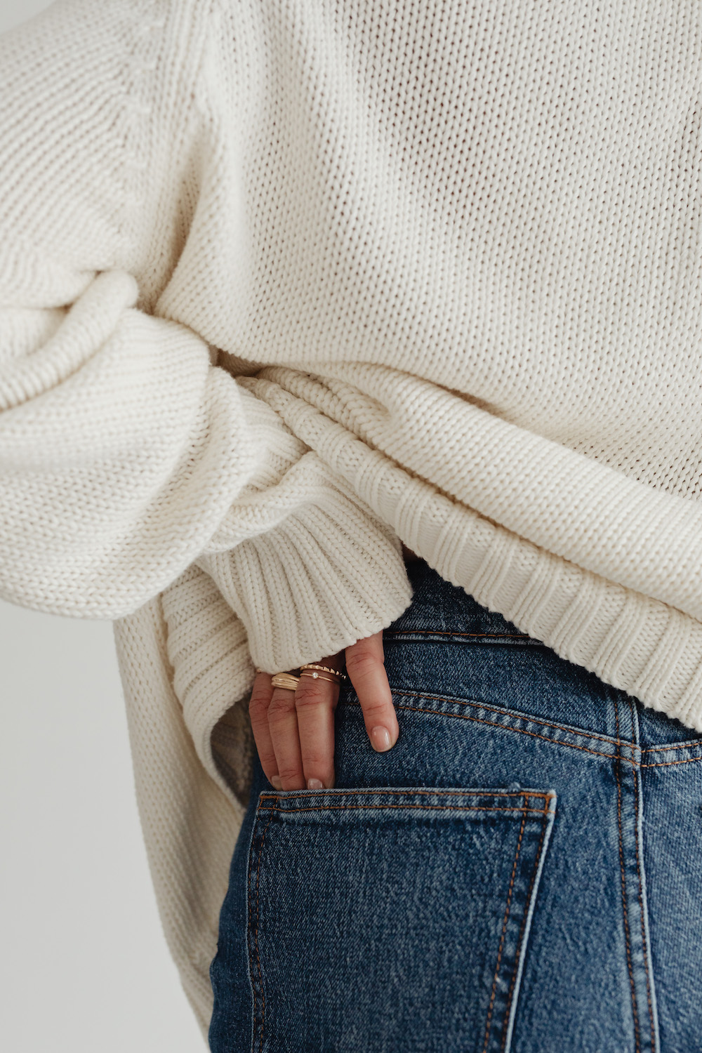 woman-in-white-sweater-gold-rings-jewelry-jeans