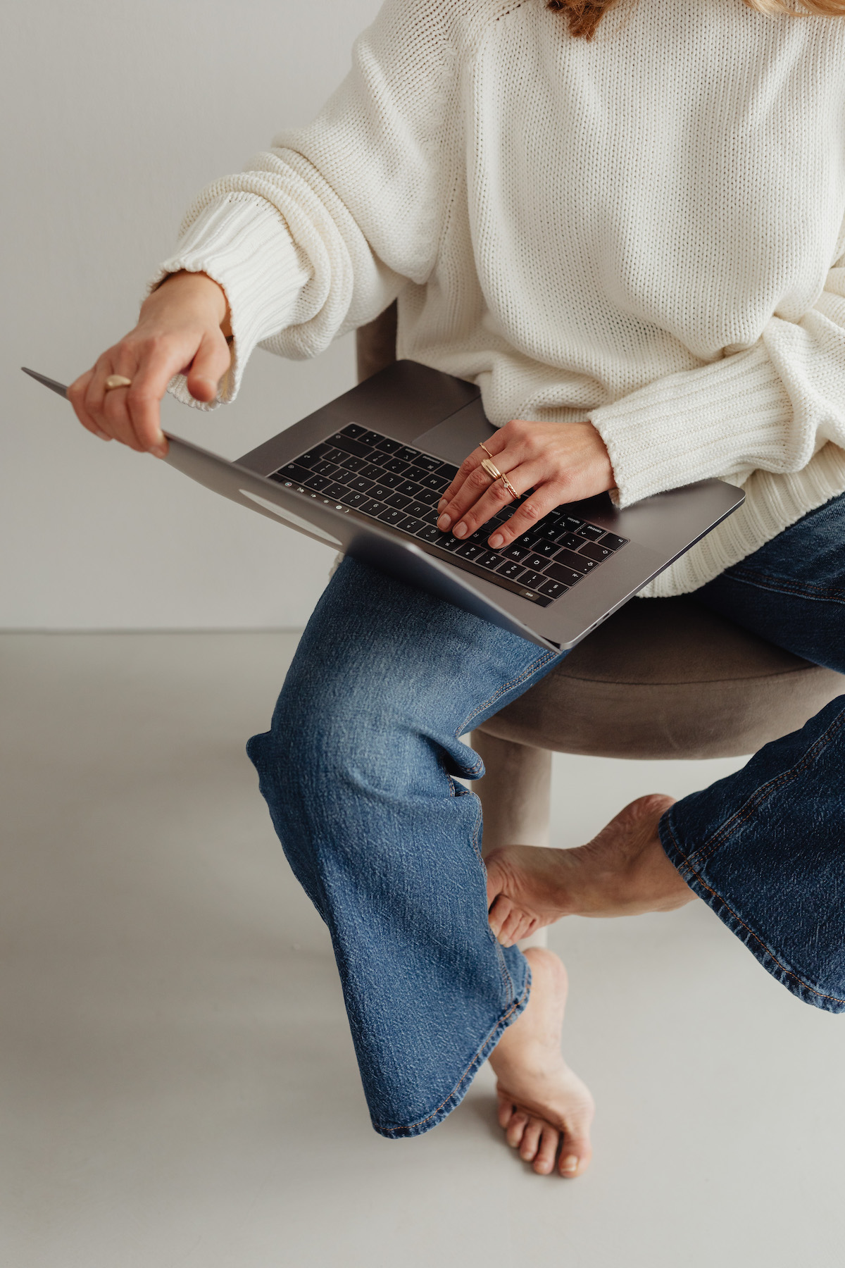 woman-in-white-sweater-gold-rings-jewelry-jeans-laptop-showit